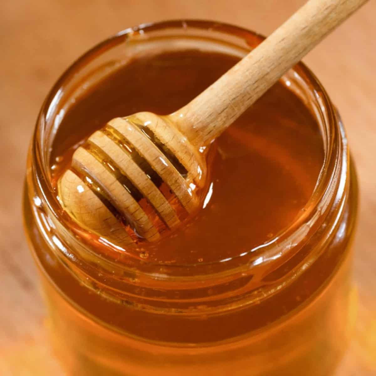 Honey dipper resting in a jar of honey on a wooden surface.