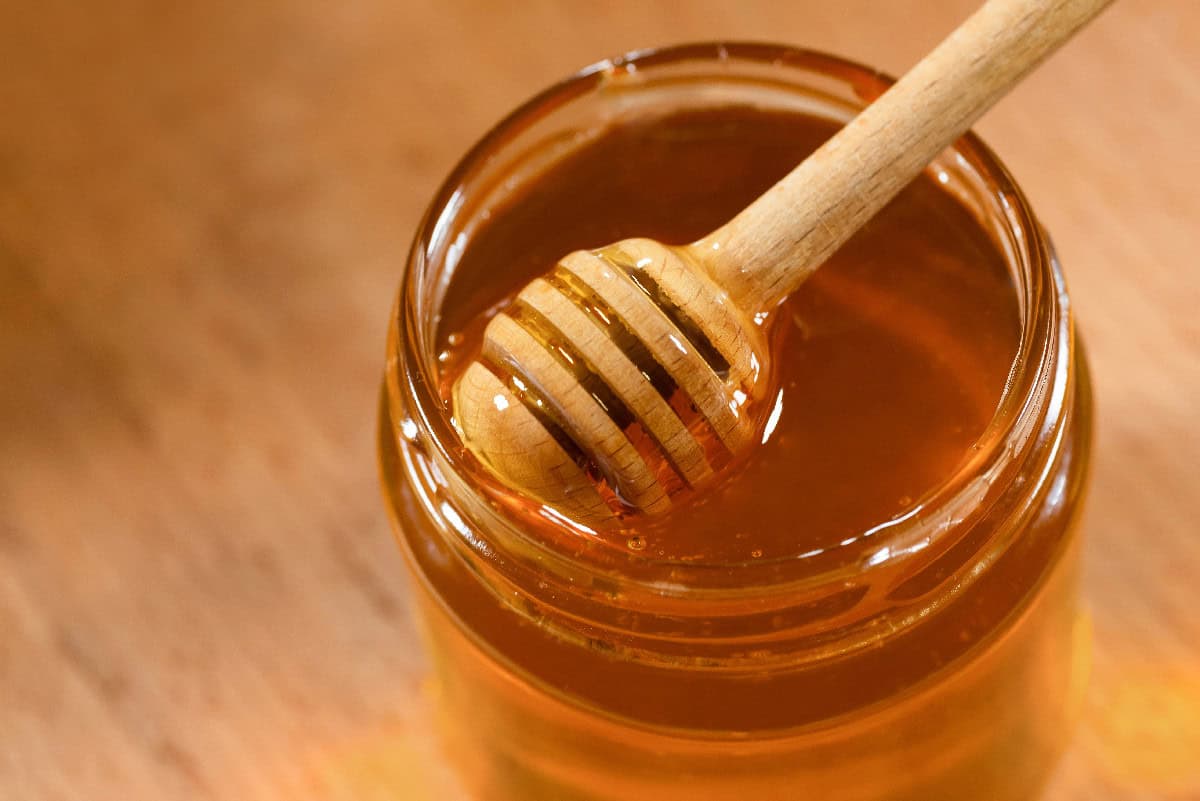 Honey dipper resting in a jar of golden honey on a wooden surface.