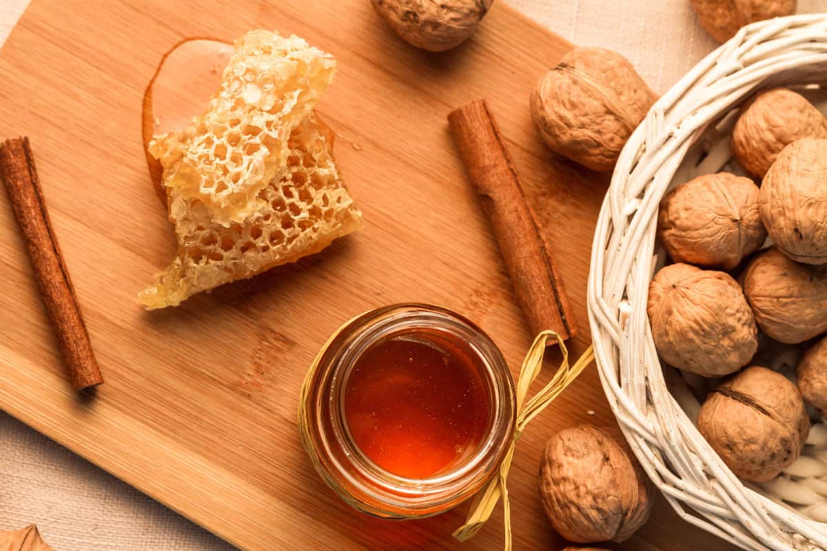 Jar of honey with honeycomb, walnuts, and cinnamon sticks on a wooden board.