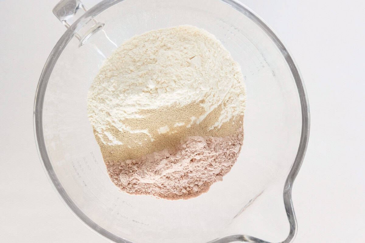 Red velvet cinnamon roll dry ingredients with flour, cake mix, and yeast in a mixing bowl.