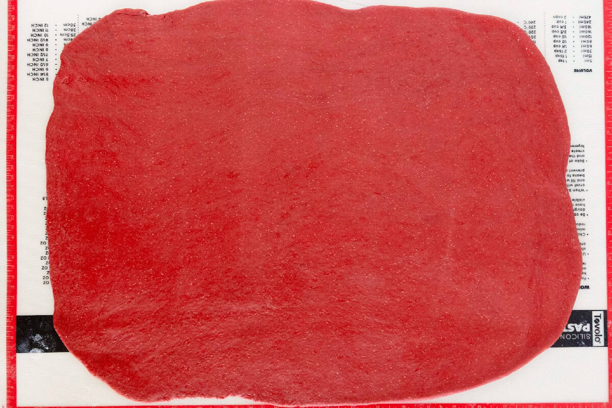 Red velvet cinnamon roll dough rolled into a large rectangle on a pastry mat.