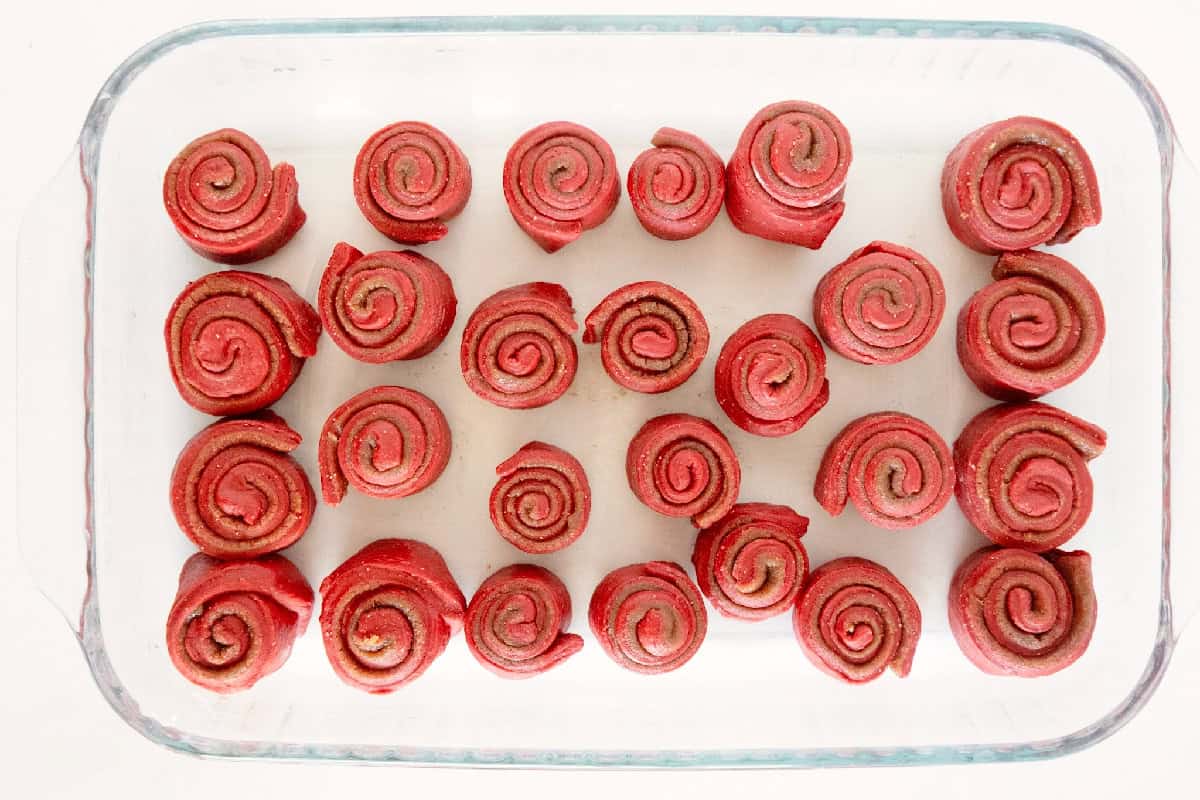 Unbaked red velvet cinnamon rolls arranged in a glass baking dish.