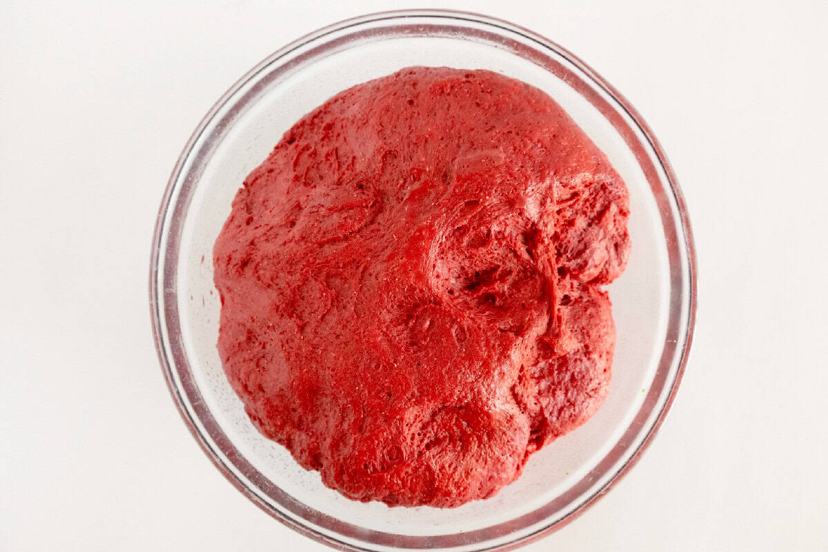 Red velvet cinnamon roll dough after rising in a glass bowl.