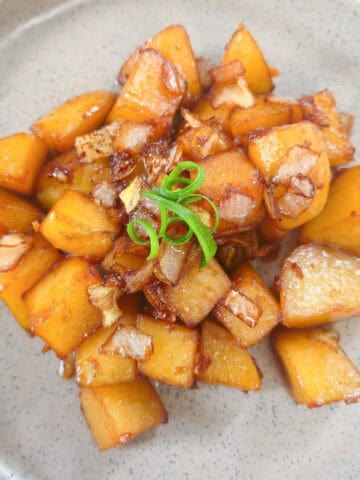 Glazed potatoes with caramelized onions and scallion strips served on a plate.