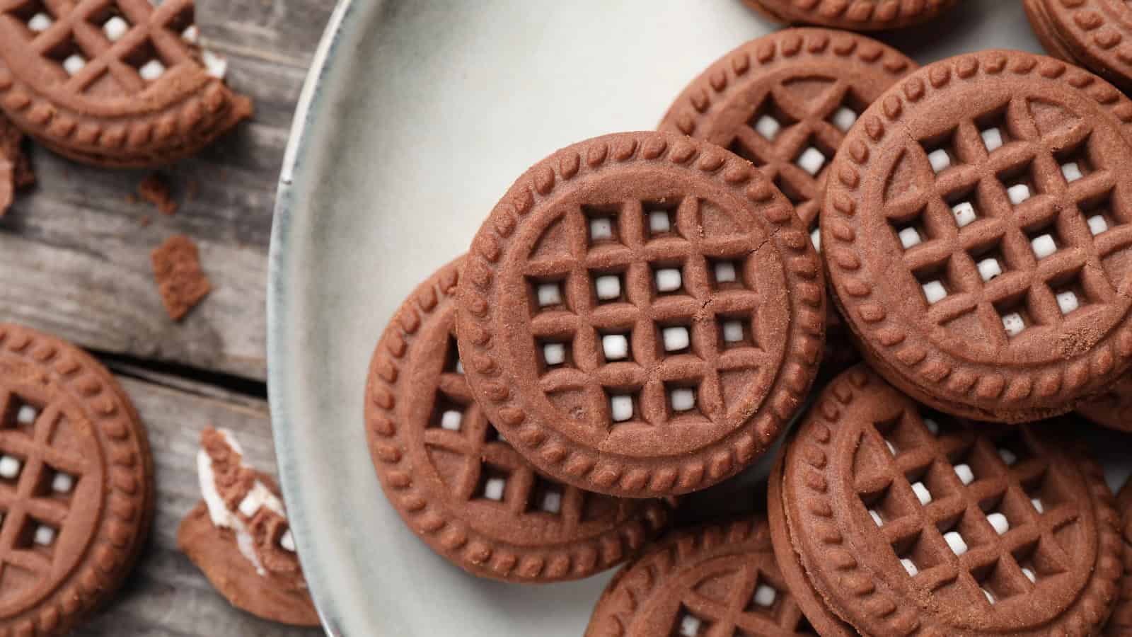 Chocolate lattice cookies arranged on a plate and wooden table.