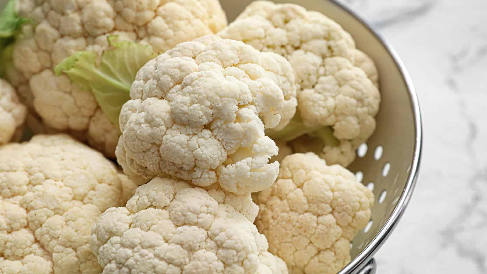 Fresh cauliflower heads in a metal colander.