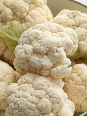 Fresh cauliflower heads resting in a metal colander.