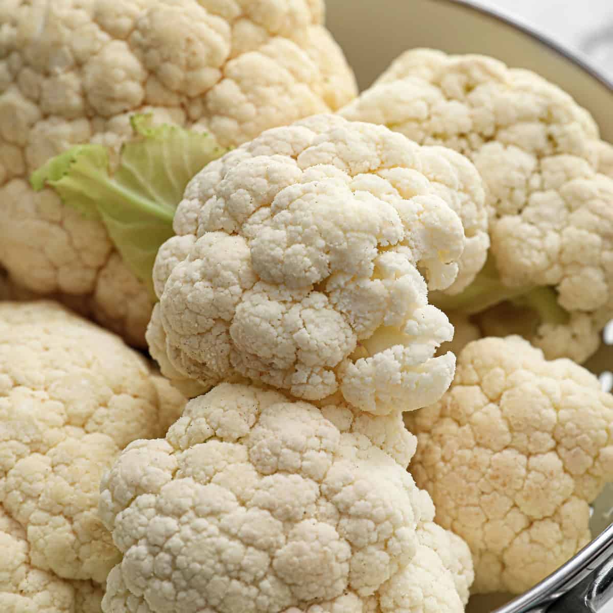 Fresh cauliflower heads resting in a metal colander.