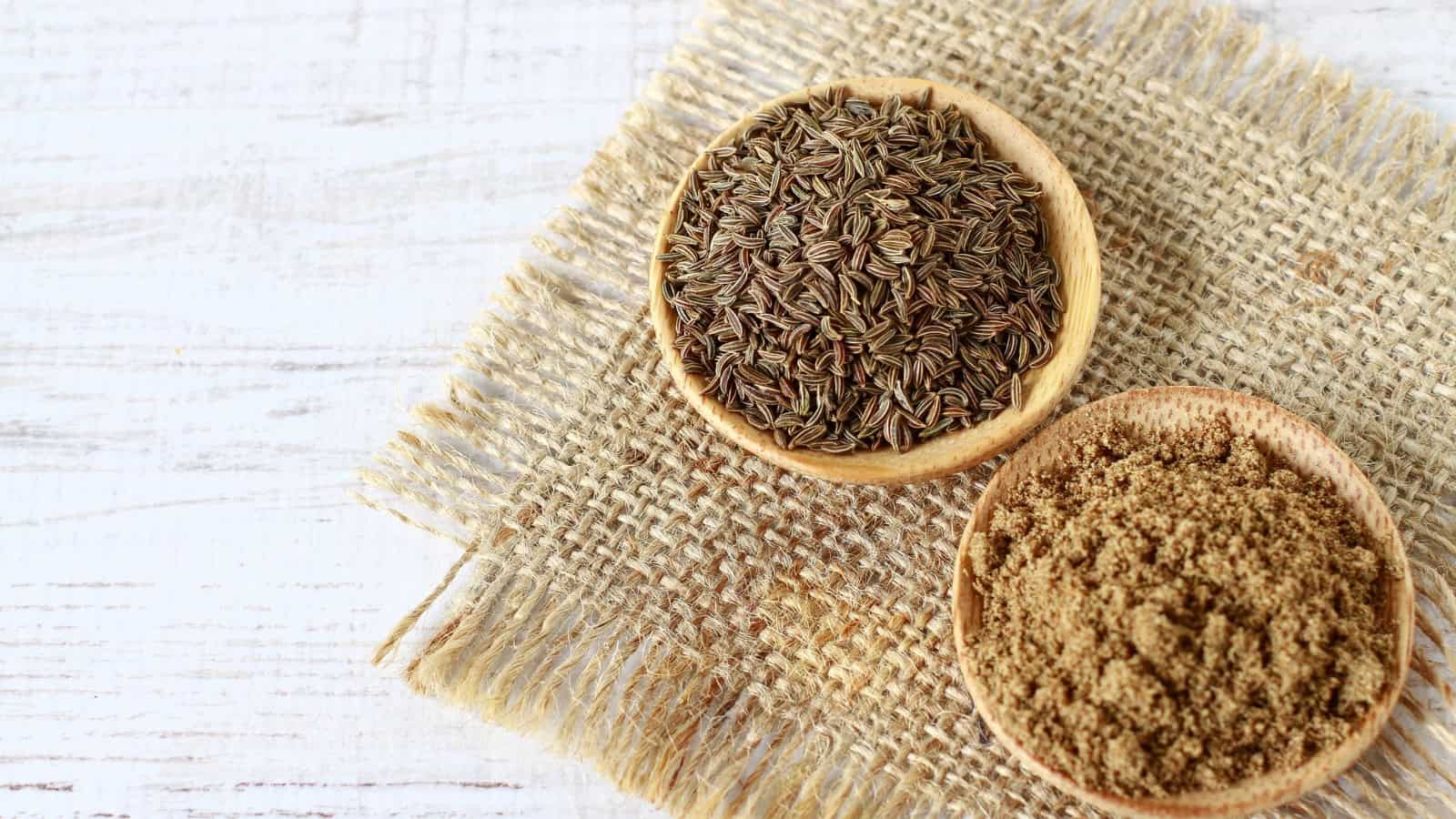 Bowls of cumin seeds and ground cumin on burlap.
