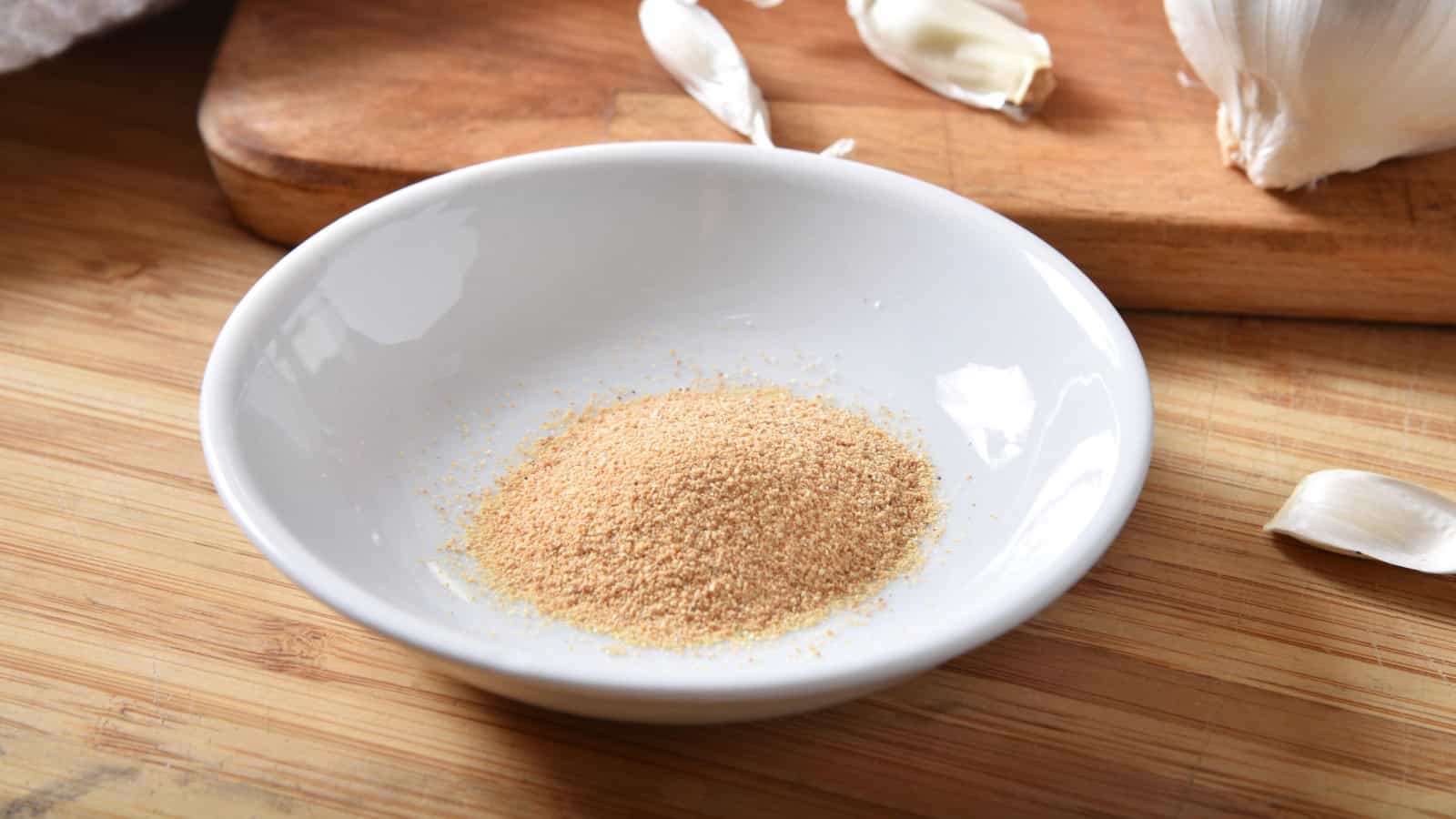 Bowl of garlic seasoning powder with fresh garlic on a wooden cutting board.