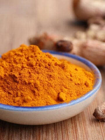 Ground turmeric in a bowl alongside fresh turmeric roots.