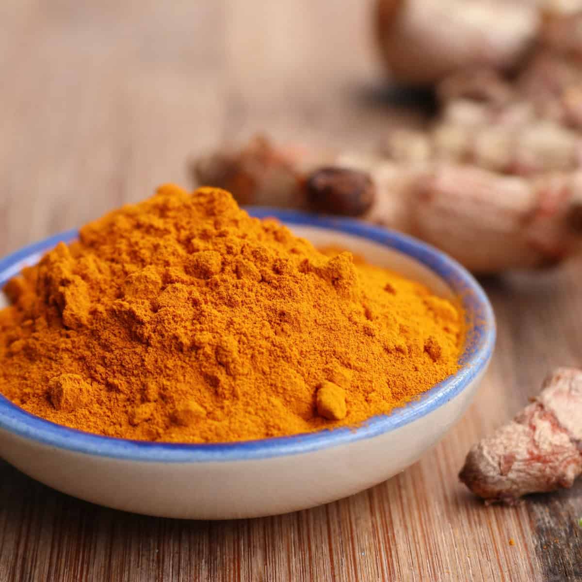 Ground turmeric in a bowl alongside fresh turmeric roots.