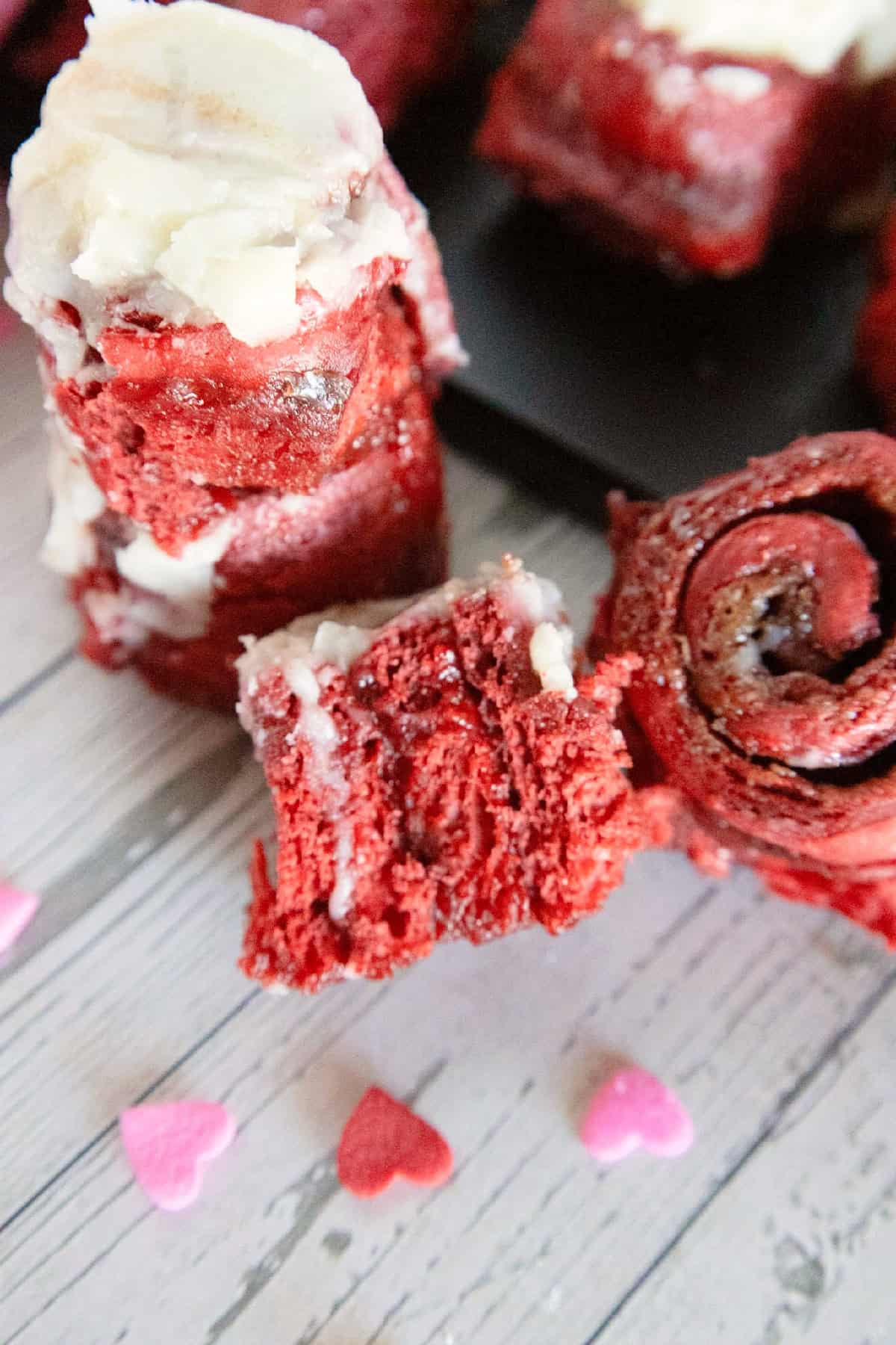 Close-up of red velvet cinnamon rolls with cream cheese frosting and heart sprinkles.