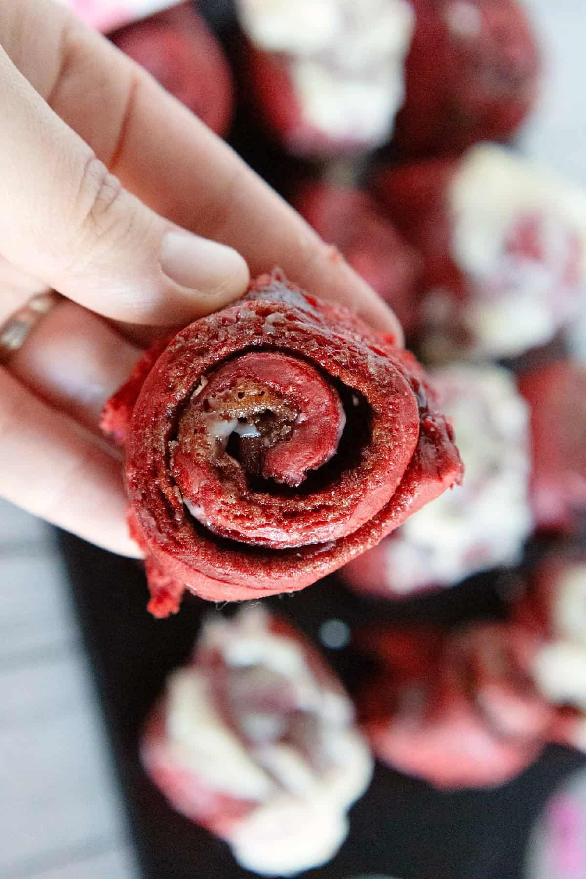 Hand holding a red velvet cinnamon roll to show the cinnamon swirl filling.