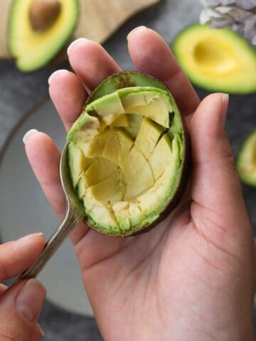 Person scooping the flesh from a halved avocado.