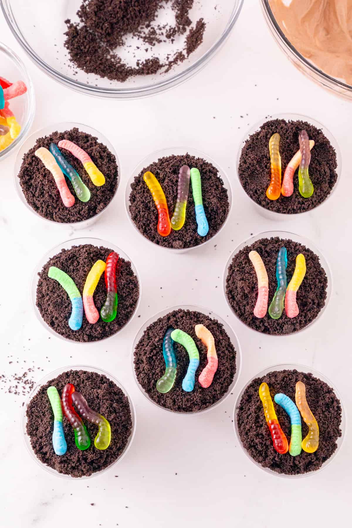 Dirt and worms pudding cups topped with Oreo crumbs and colorful gummy worms.