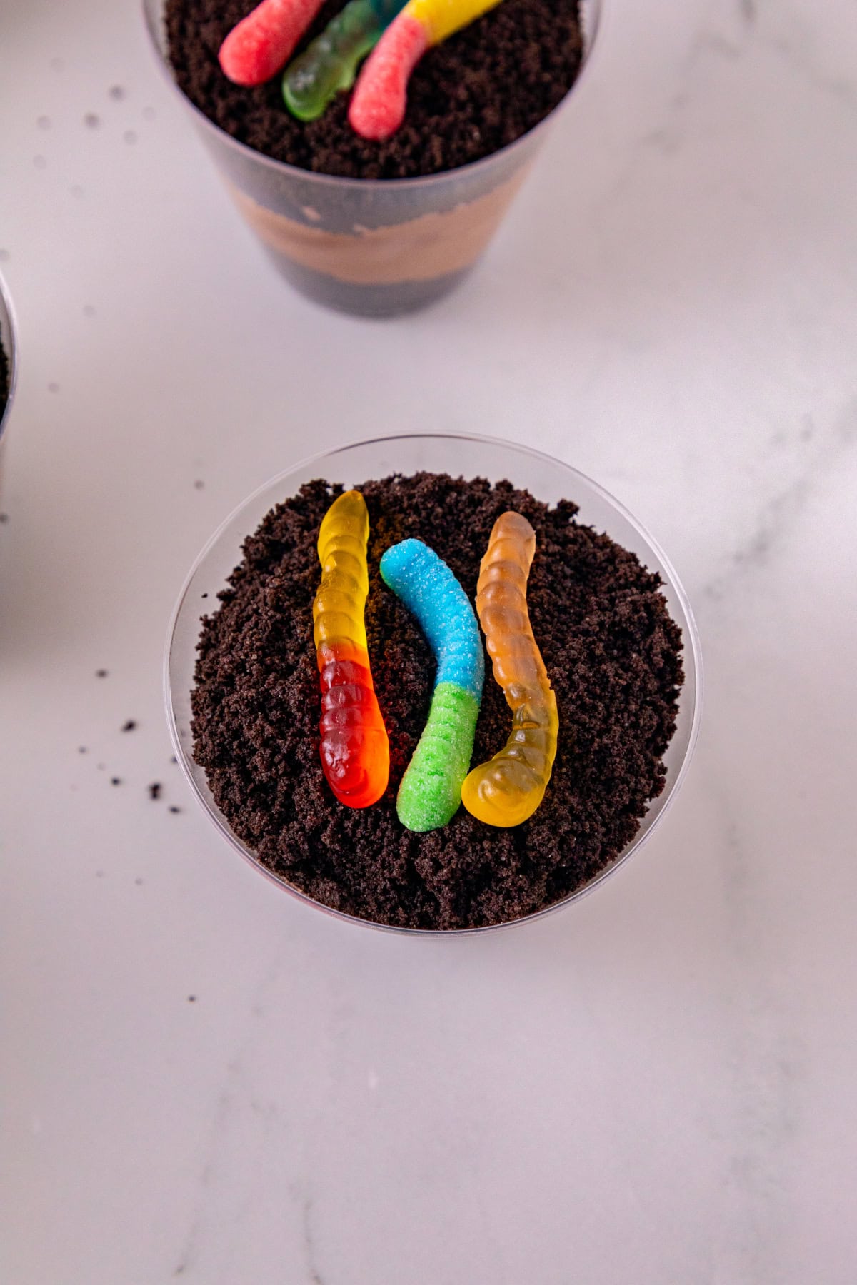 Close-up of a dirt and worms pudding cup topped with Oreo crumbs and three colorful gummy worms.
