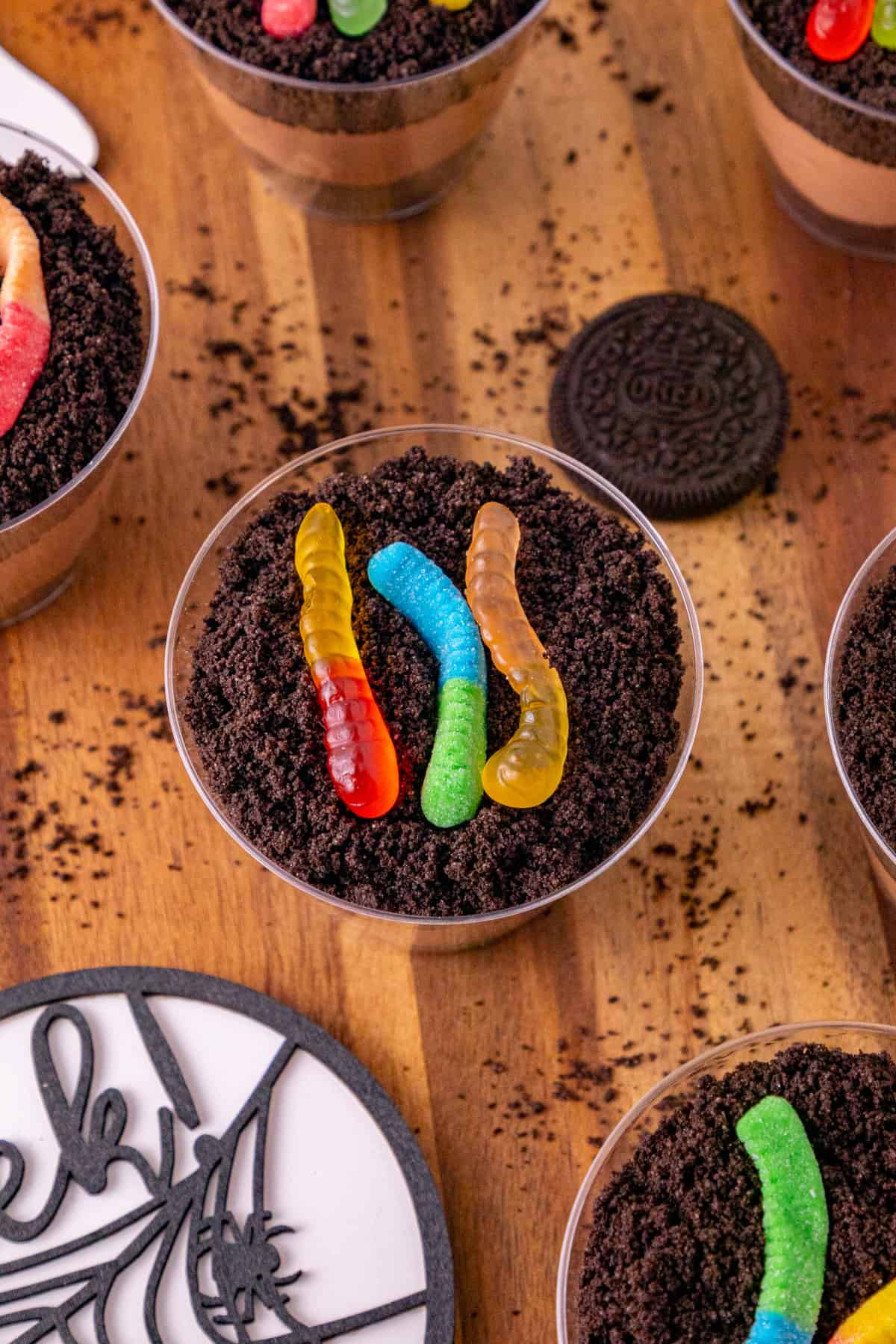 Close-up of a dirt and worms pudding cup topped with crushed Oreos and three colorful gummy worms.