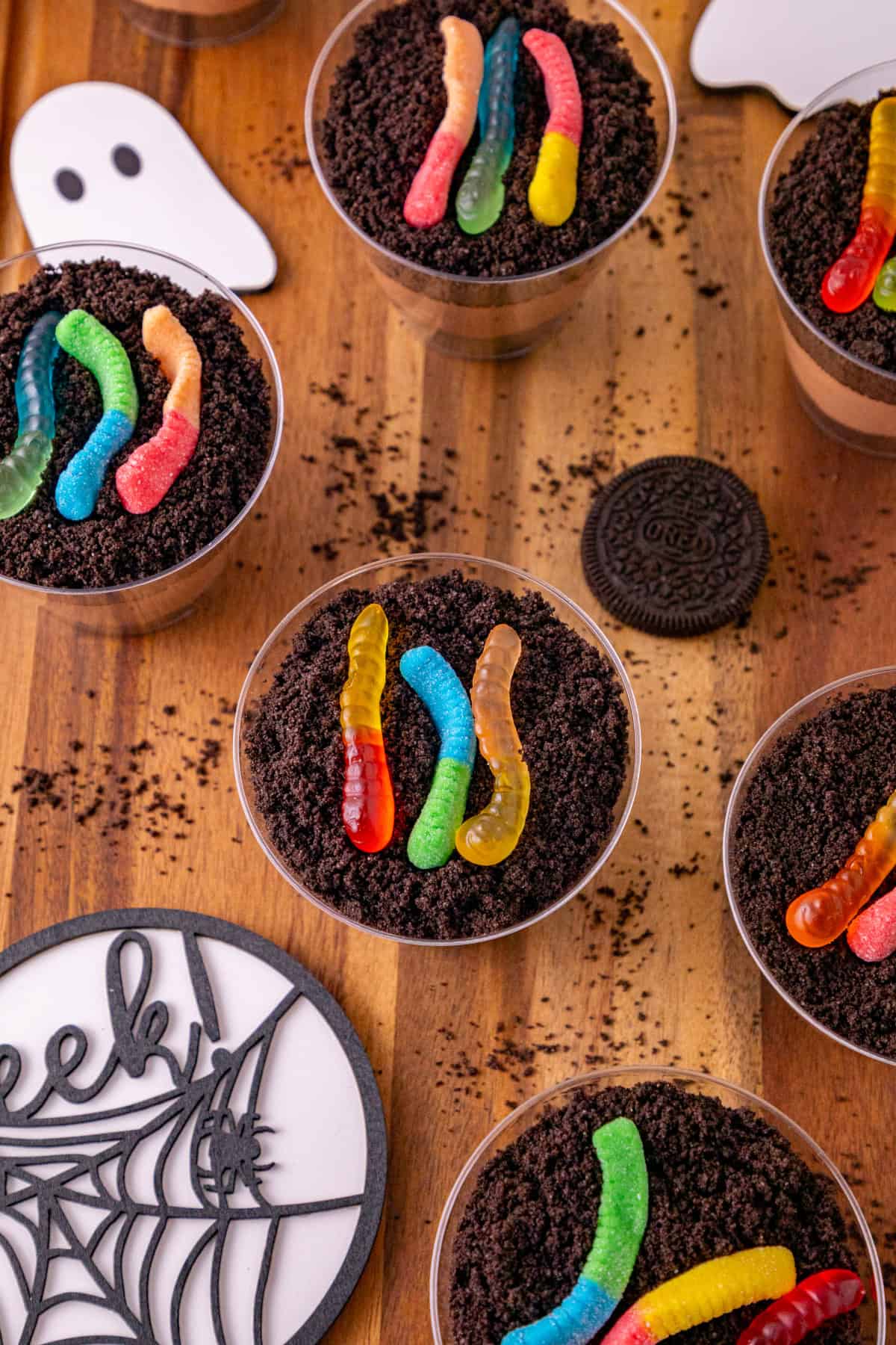 Dirt and worms pudding cups with Oreo crumbs and gummy worms arranged with Halloween ghost decorations.