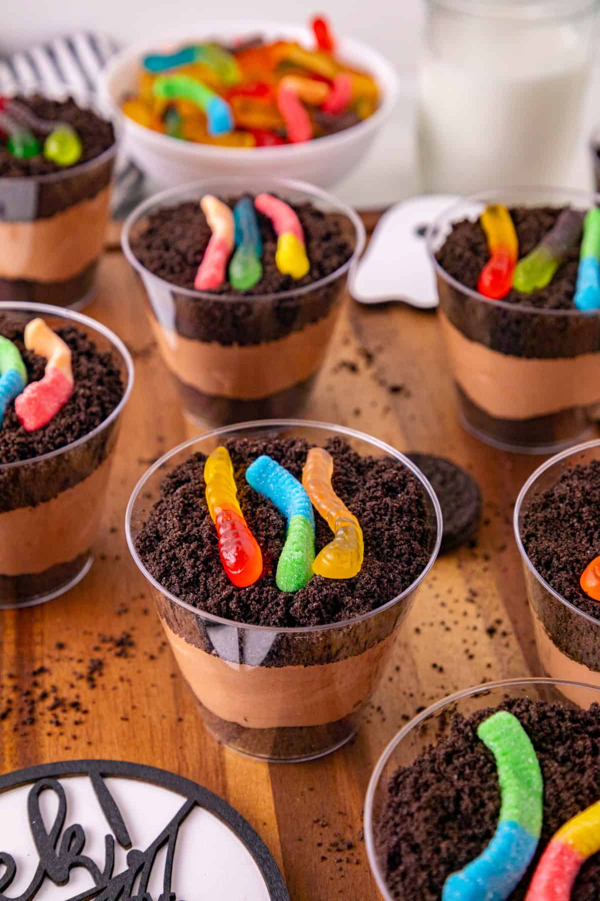 Layered dirt and worms pudding cups topped with Oreo crumbs and colorful gummy worms.
