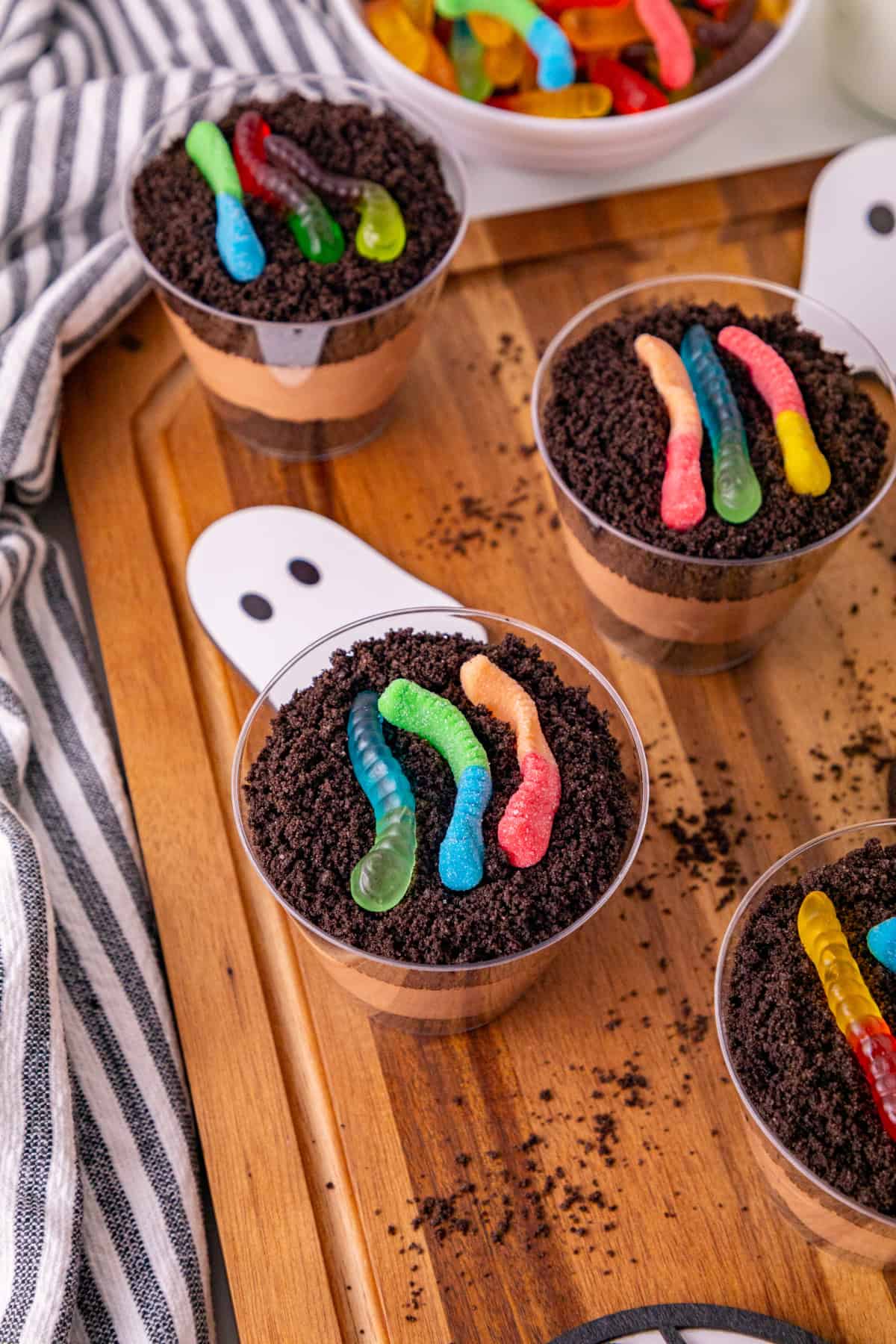 Colorful gummy worms in chocolate dessert cups with crushed cookies.