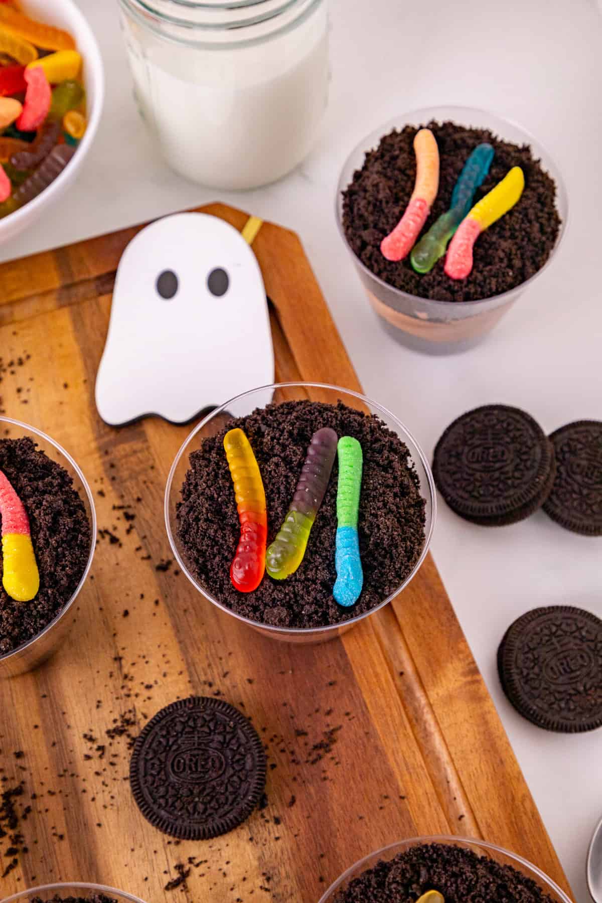 Halloween dirt and worms pudding cups with Oreo crumbs, gummy worms, ghost decorations, and cookies.
