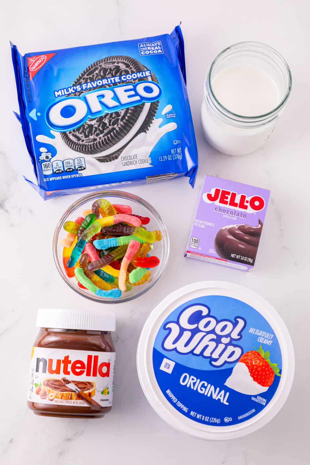 Ingredients for dirt and worms pudding cups with Oreos, chocolate pudding mix, milk, Nutella, Cool Whip, and gummy worms.